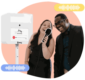 Two happy people holding a microphone in front of a KRUU photo booth, using the audio feature.