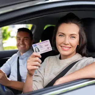 Woman seating on the driving seat of a car, holding a driver's license.