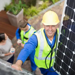 Expert professional solar panel installer carrying solar panel to the roof of a house.