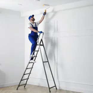 Expert professional painter standing on a ladder painting the ceiling of a room.