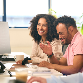 A man and a woman look at a monitor and laugh