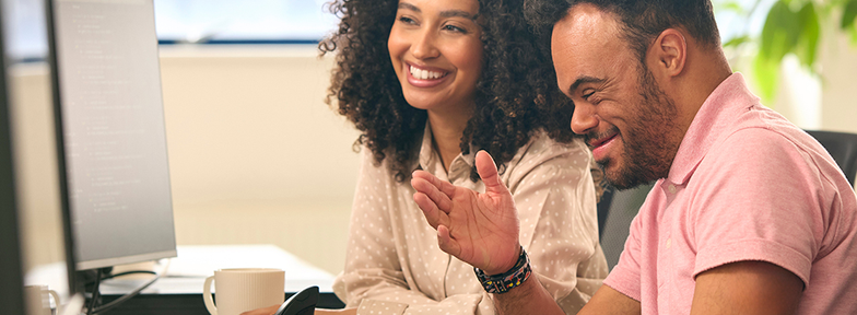 A man and a woman look at a monitor and laugh