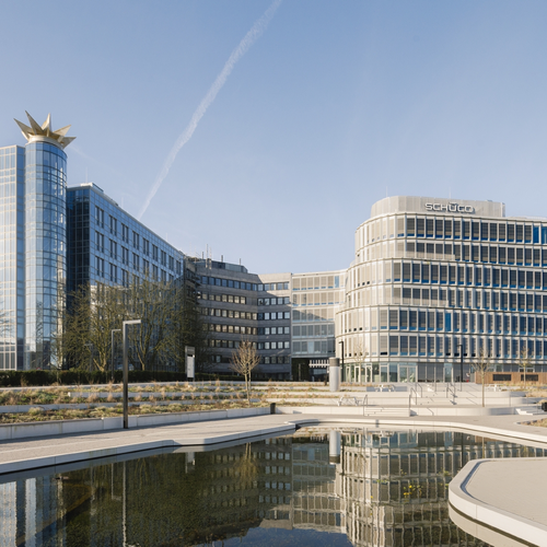 Modern office building with glass facade, curved structure, and a star-shaped sculpture on the roof, reflected in a nearby pond.