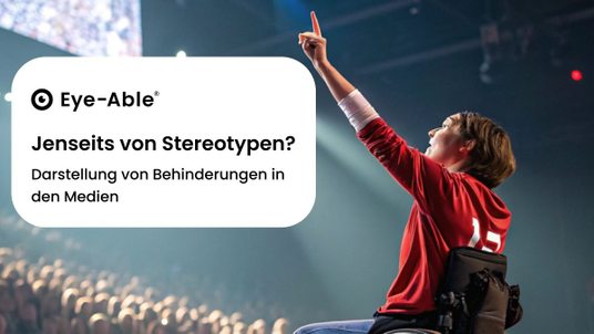 A person in a wheelchair has thrown a ball into the air with their left hand. The ball is already in the air and the person is pointing upwards with their left index finger. In the background, the crowd in a stadium applauds while a sporting event is shown on a large screen. The person is wearing a red sports jersey.