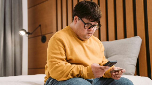 A man with Down syndrome using a smartphone in a modern hotel room