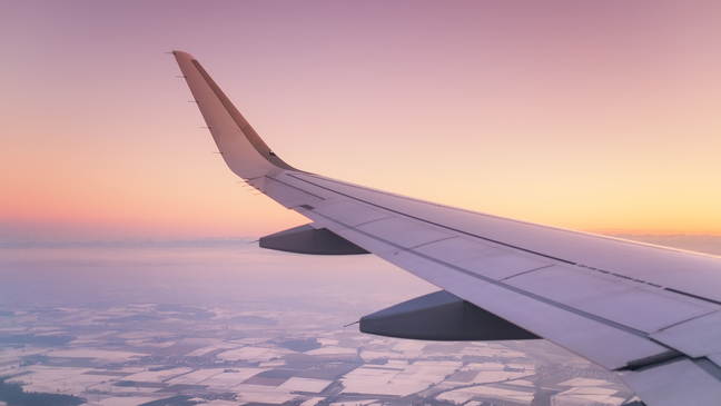 View from airplane window with wing during sunset flight over landscape