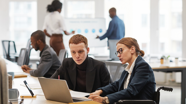 Business team discussing a project, including a person in a wheelchair using a laptop