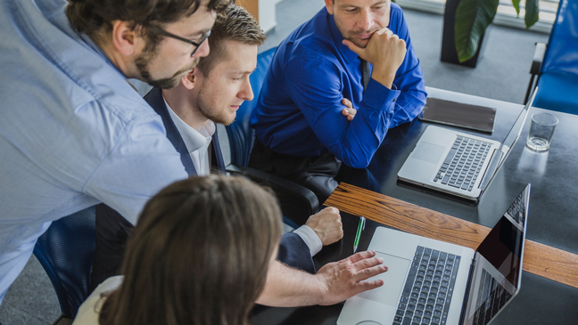 Team collaborating around a laptop at a table.