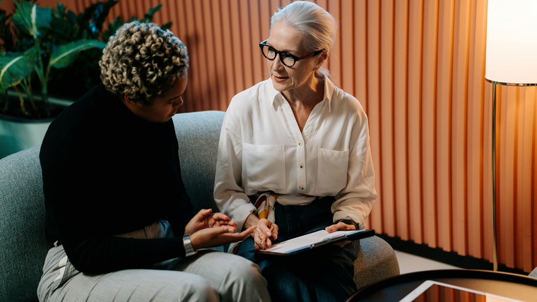 Two women having a discussion, one holding a notebook, in an accessible office space