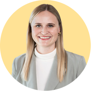 Smiling person with long blonde hair, wearing a gray blazer and white top, against a yellow circular background.