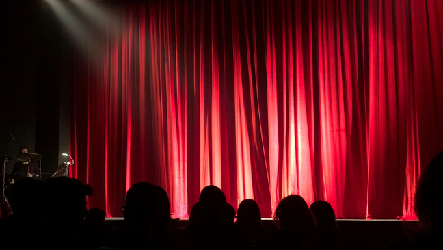 Audience waiting for a performance in front of a red curtain on stage