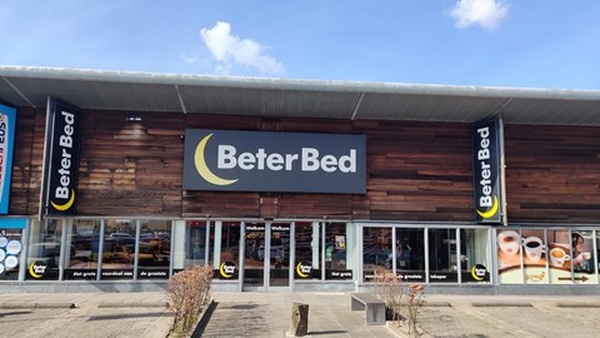 Exterior of a Beter Bed store with a wooden facade, large display windows, and the Beter Bed logo prominently displayed above the entrance.