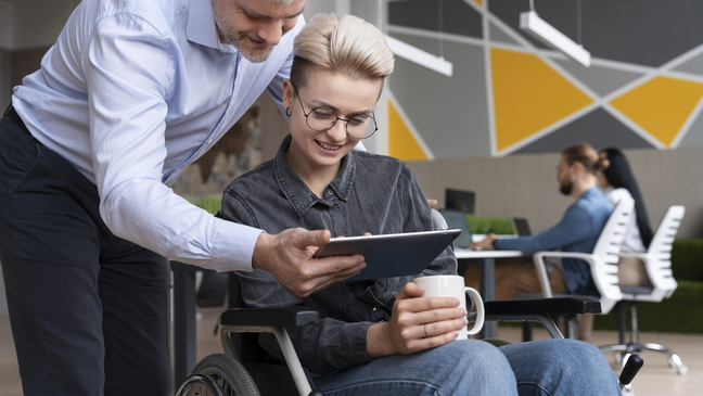 Man showing a tablet to a woman in a wheelchair during a work discussion
