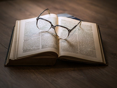 Eine Brille liegt auf einem aufgeschlagenen Buch.