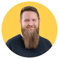 Man with a long beard and short hair, wearing a black shirt, smiles against a yellow circular background.