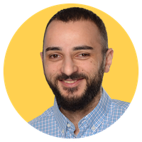 Smiling man with a beard in a blue checkered shirt against a yellow circular background.