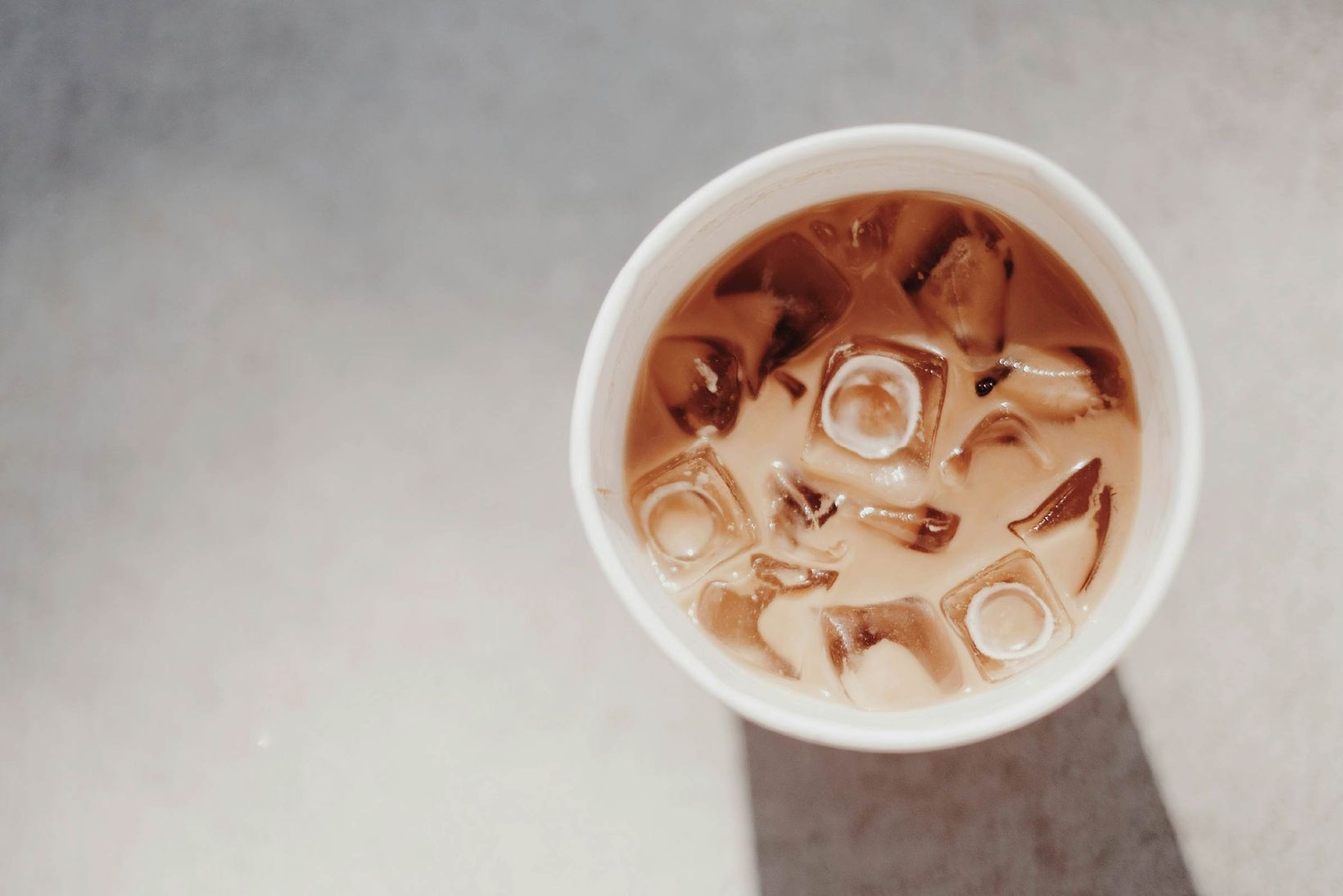 A view from above of a white cup filled with iced coffee on a marble background