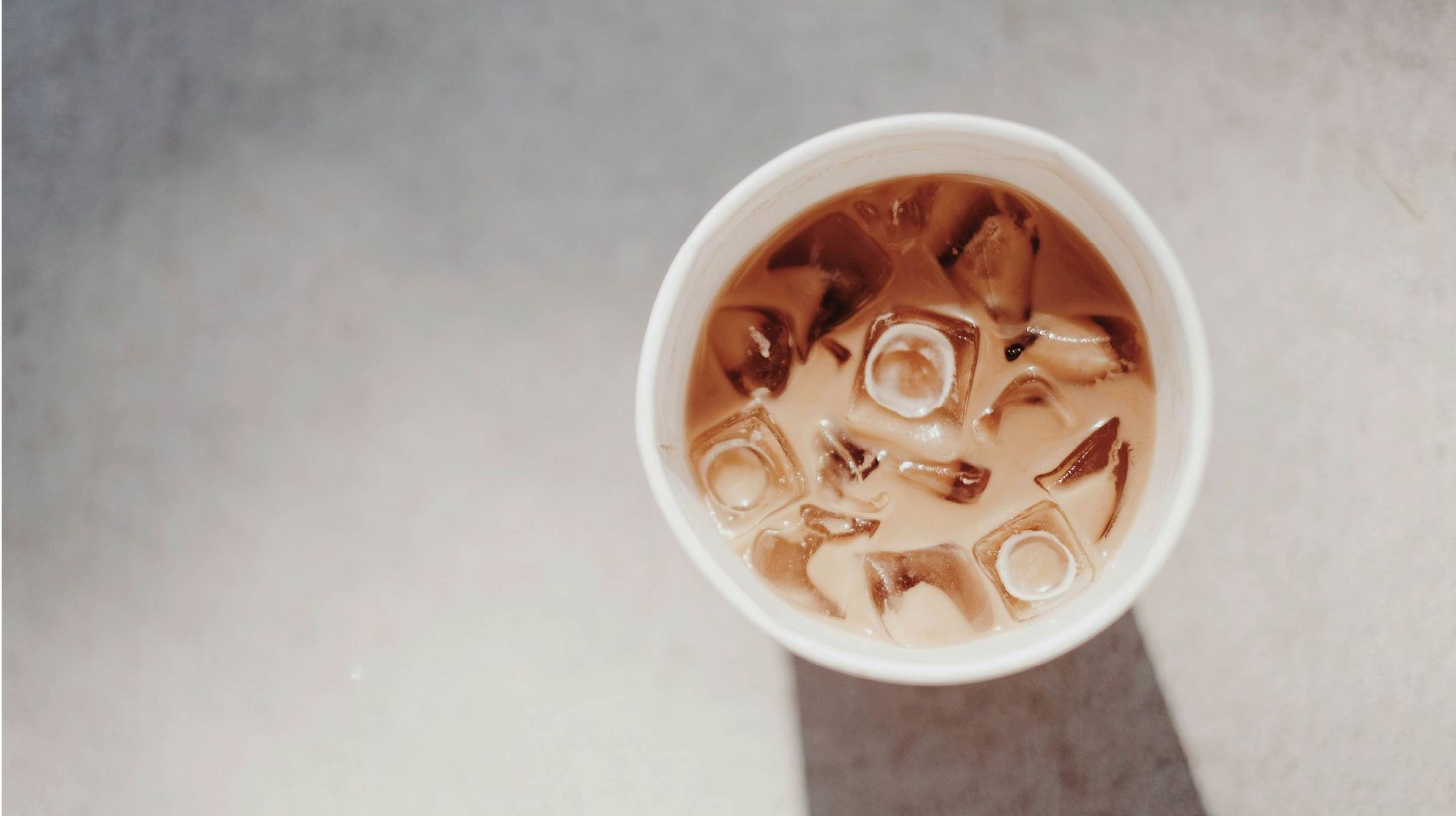 A view from above of a white cup filled with iced coffee on a marble background