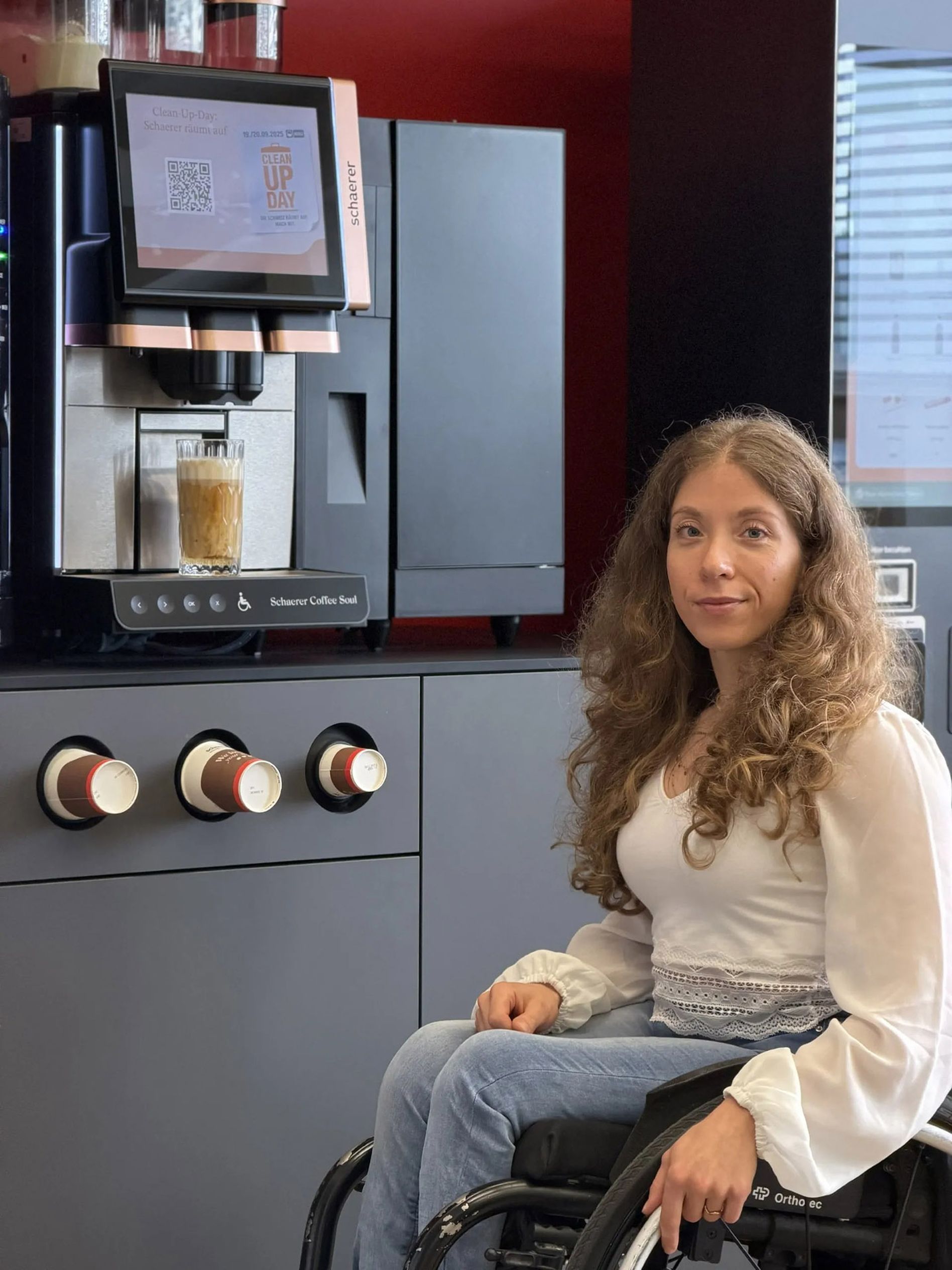 Licia Mussinelli in her wheelchair in front of a coffee machine with accessbility feature "Easy Access"