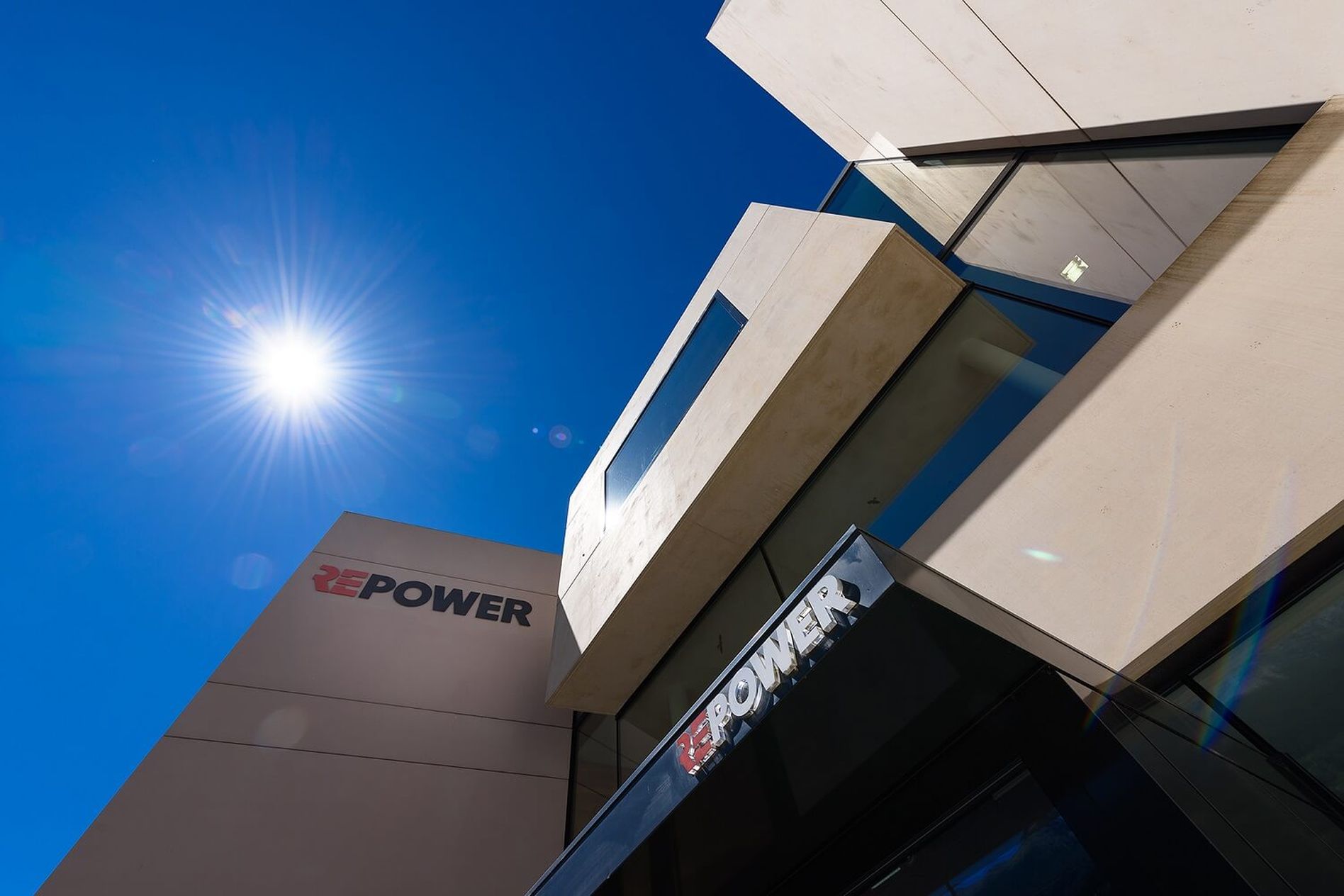 Modern building with angular design against a clear blue sky, sun shining brightly. "REPOWER" logo visible on the building facade.