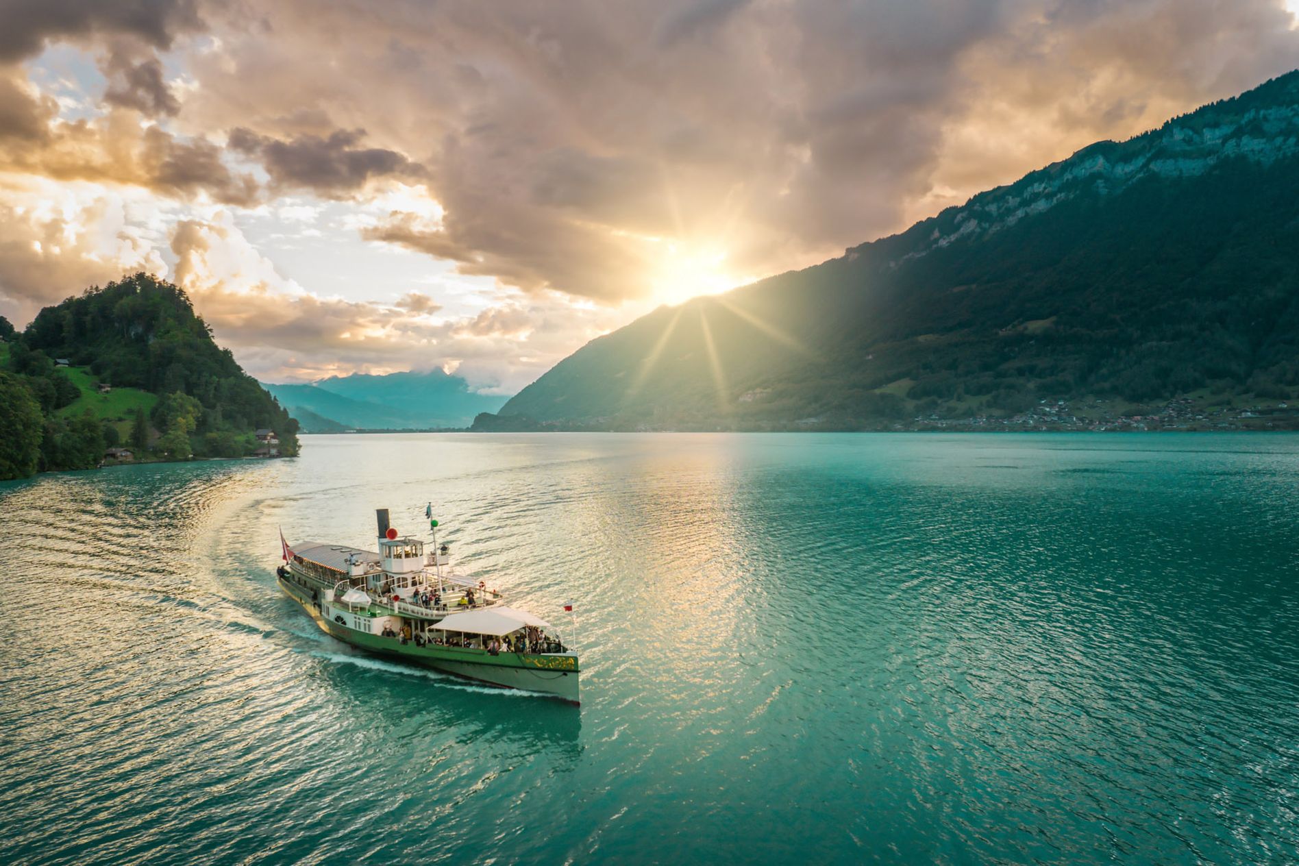 A boat sails on a lake Brienz surrounded by mountains, with the sun setting and casting a warm glow over the scene