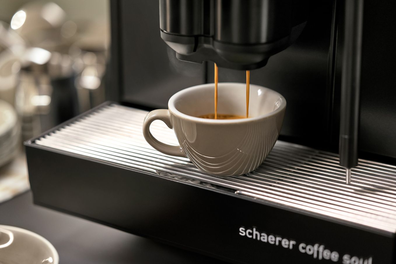 Espresso machine brewing coffee into a white cup on a drip tray, with "Schaerer Coffee Soul" branding visible.