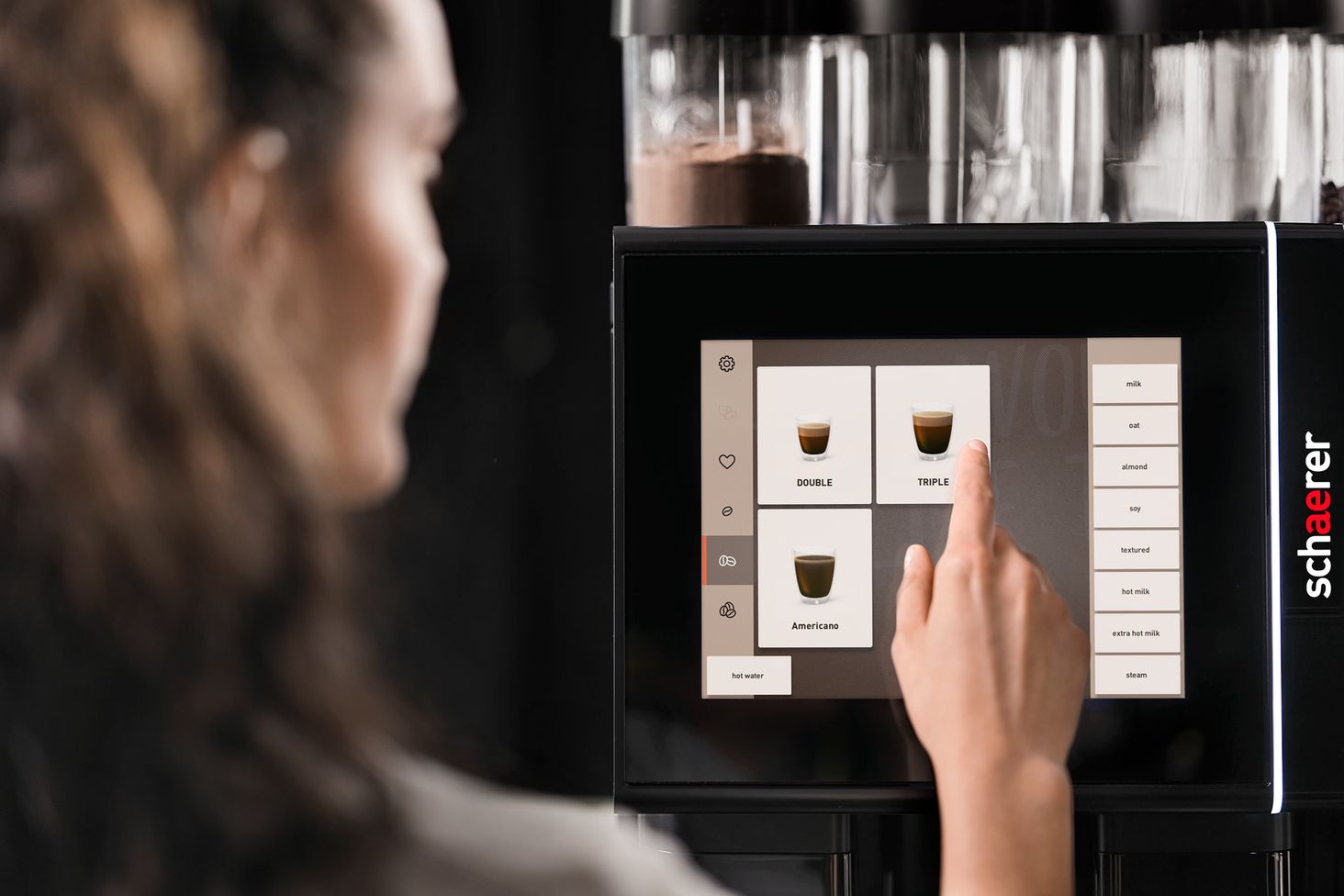Person selecting a coffee option on a touchscreen of a Schaerer coffee machine, with various drink choices displayed.