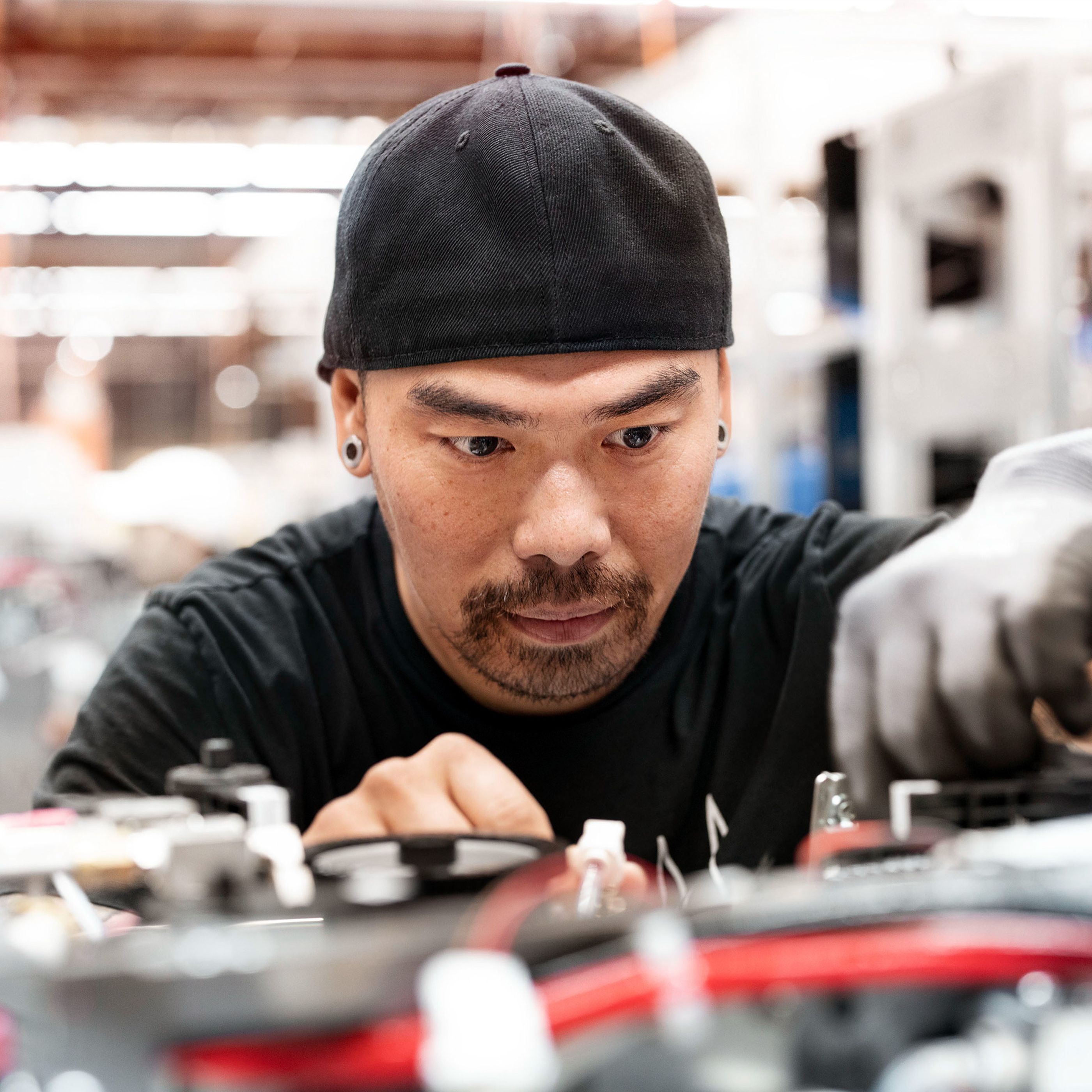 Man in a black cap and gloves focused on assembling machinery in a factory