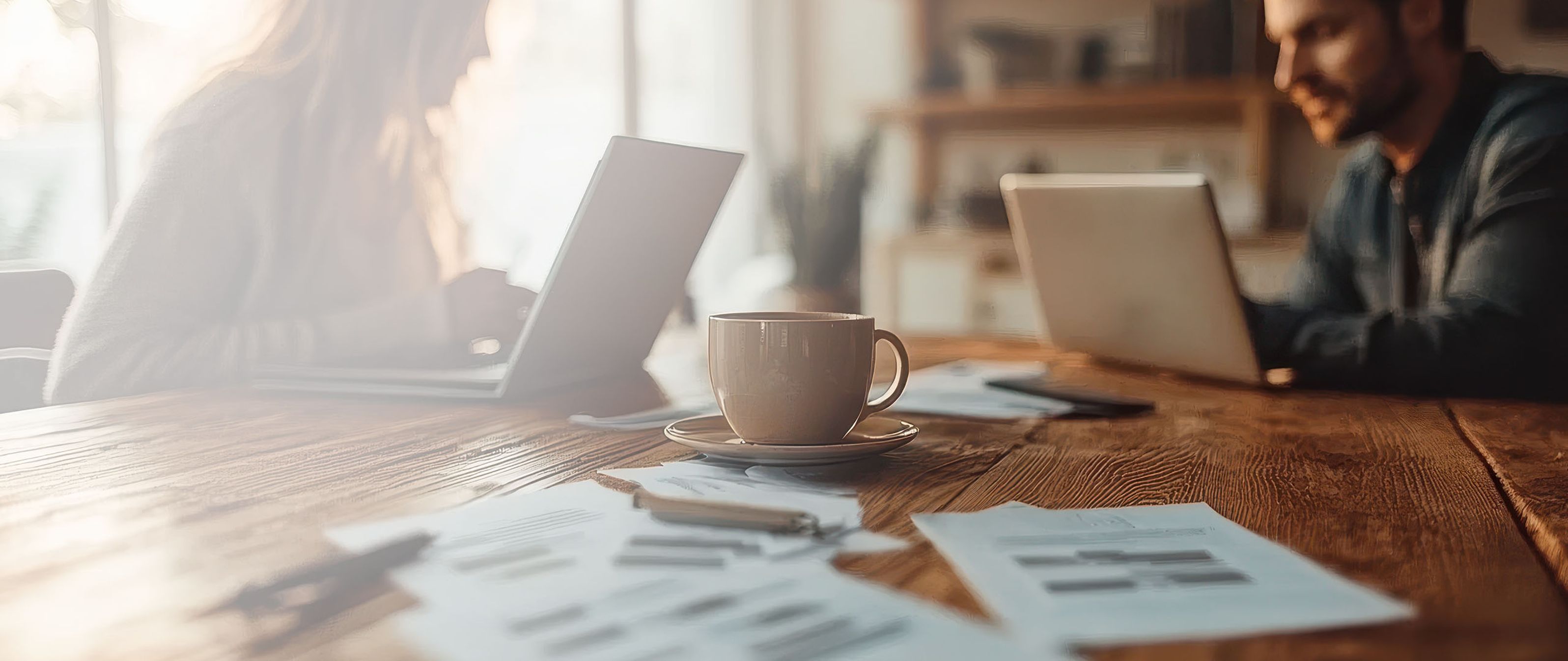 Two people reviewing documents with charts and graphs at a desk, one pointing with a pen, and a laptop nearby.