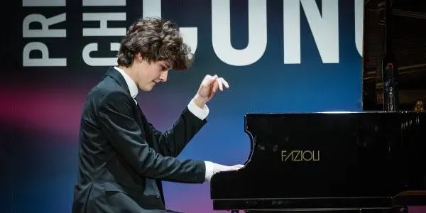 Two musicians perform on stage; a pianist on the left and a flutist on the right, in front of a sign reading "Prinses Christina Concours."