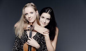 Merel Vercammen (holding her violin) and Dina Ivanova posing in front of a grey wall