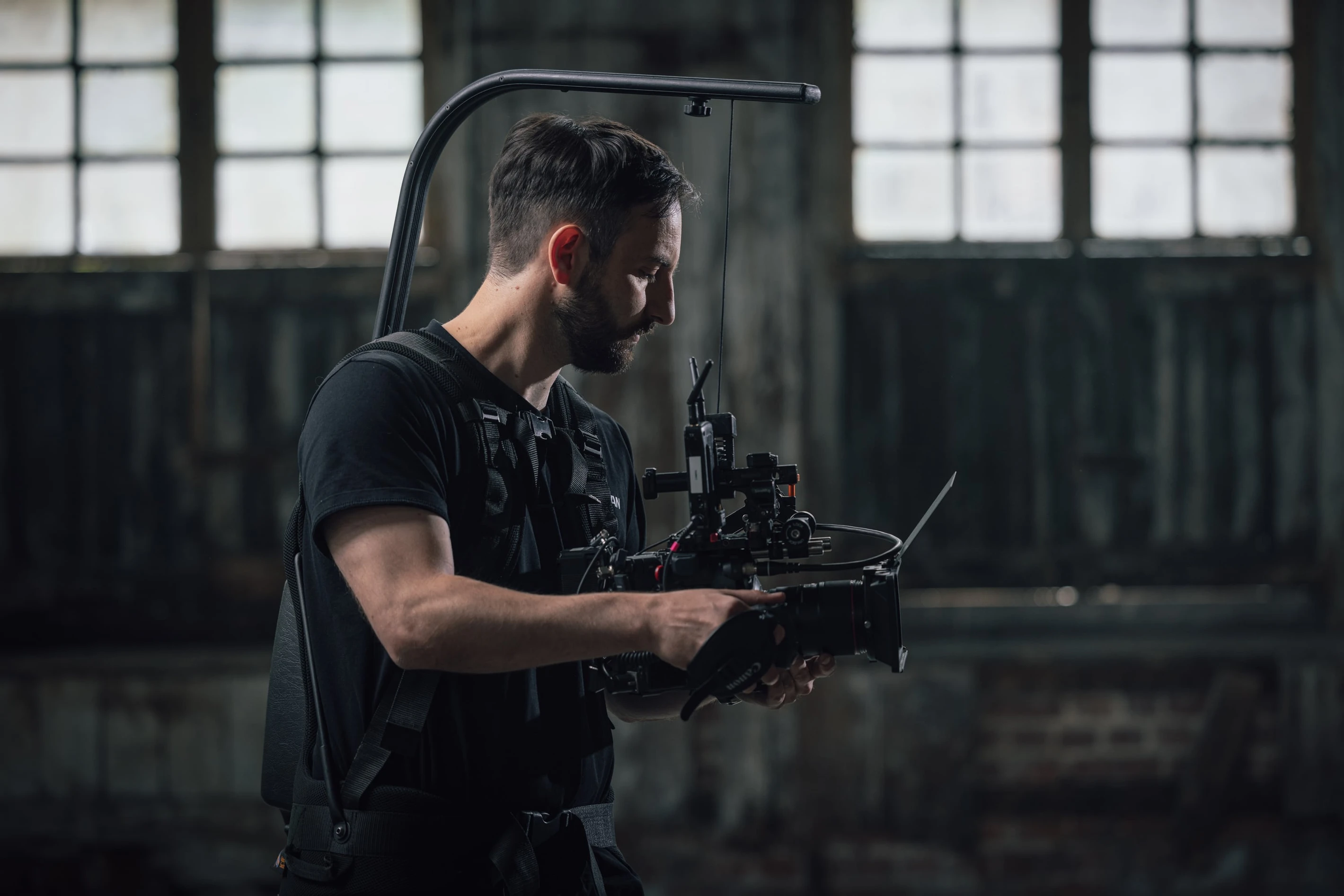 Cameraperson operating a professional stabilizing rig in a dimly lit industrial setting, focused on capturing footage.