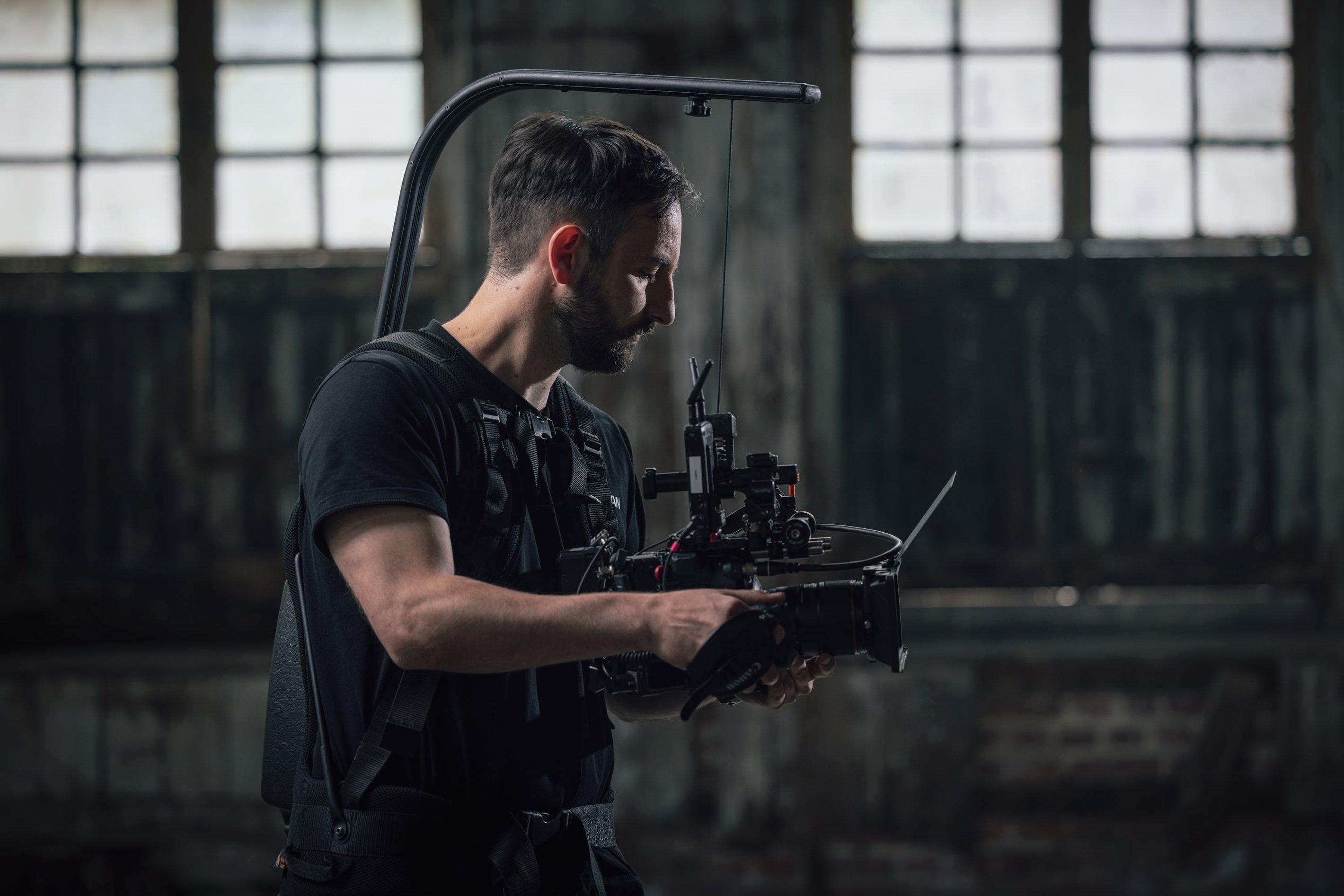 Cameraperson operating a professional stabilizing rig in a dimly lit industrial setting, focused on capturing footage.