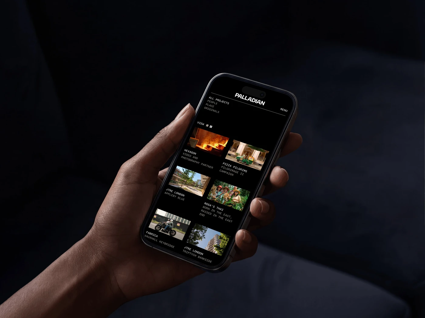 Hand holding a smartphone displaying a media app interface with various video thumbnails against a dark background.