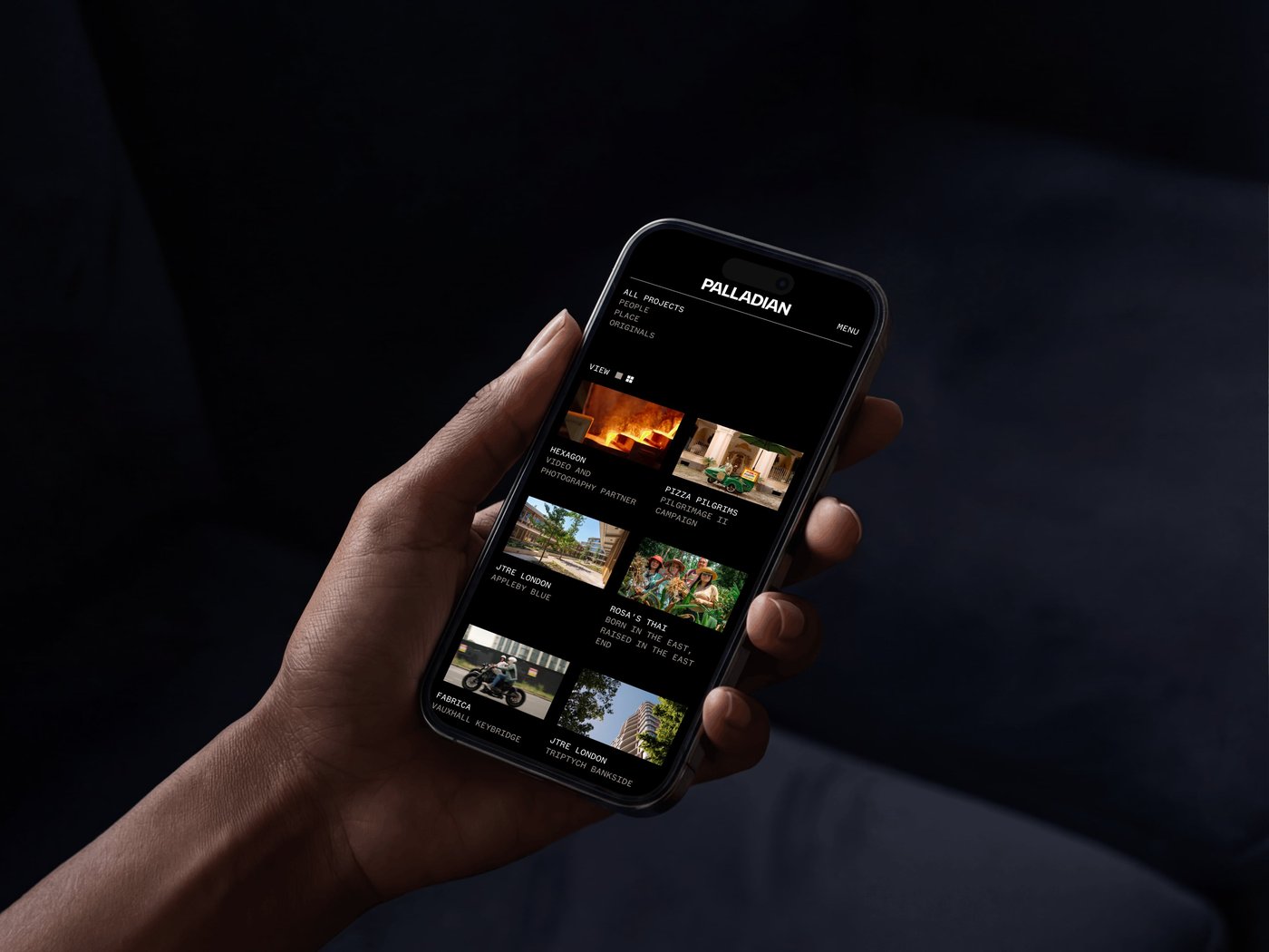 Hand holding a smartphone displaying a media app interface with various video thumbnails against a dark background.