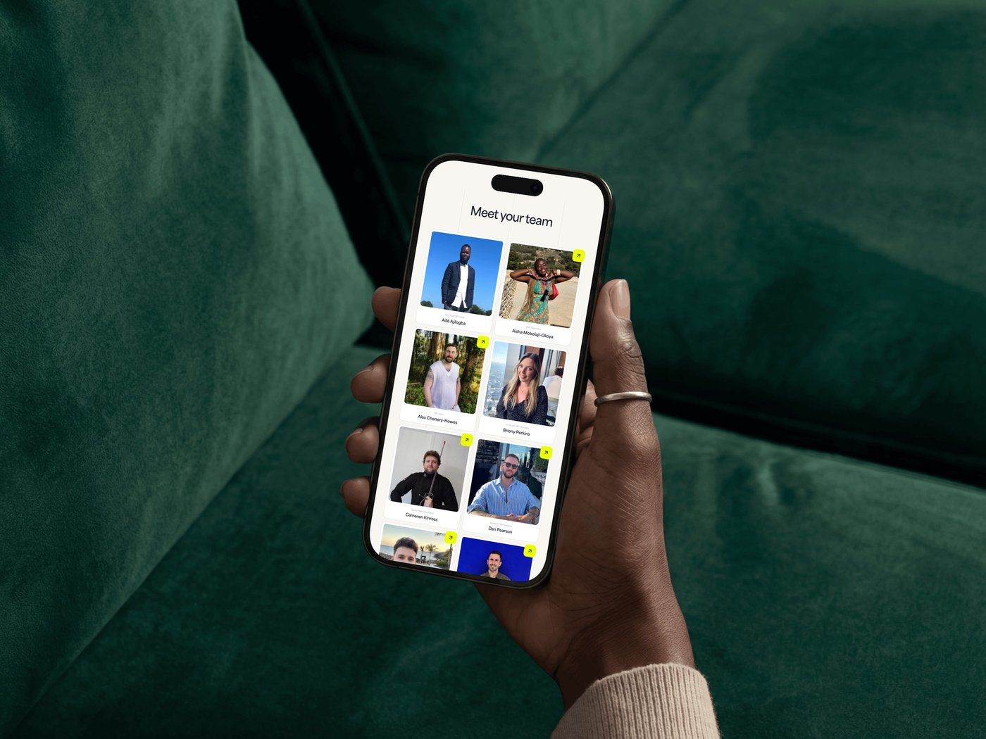 Person holding a smartphone displaying a "Meet your team" screen with photos of nine individuals on a green sofa background.