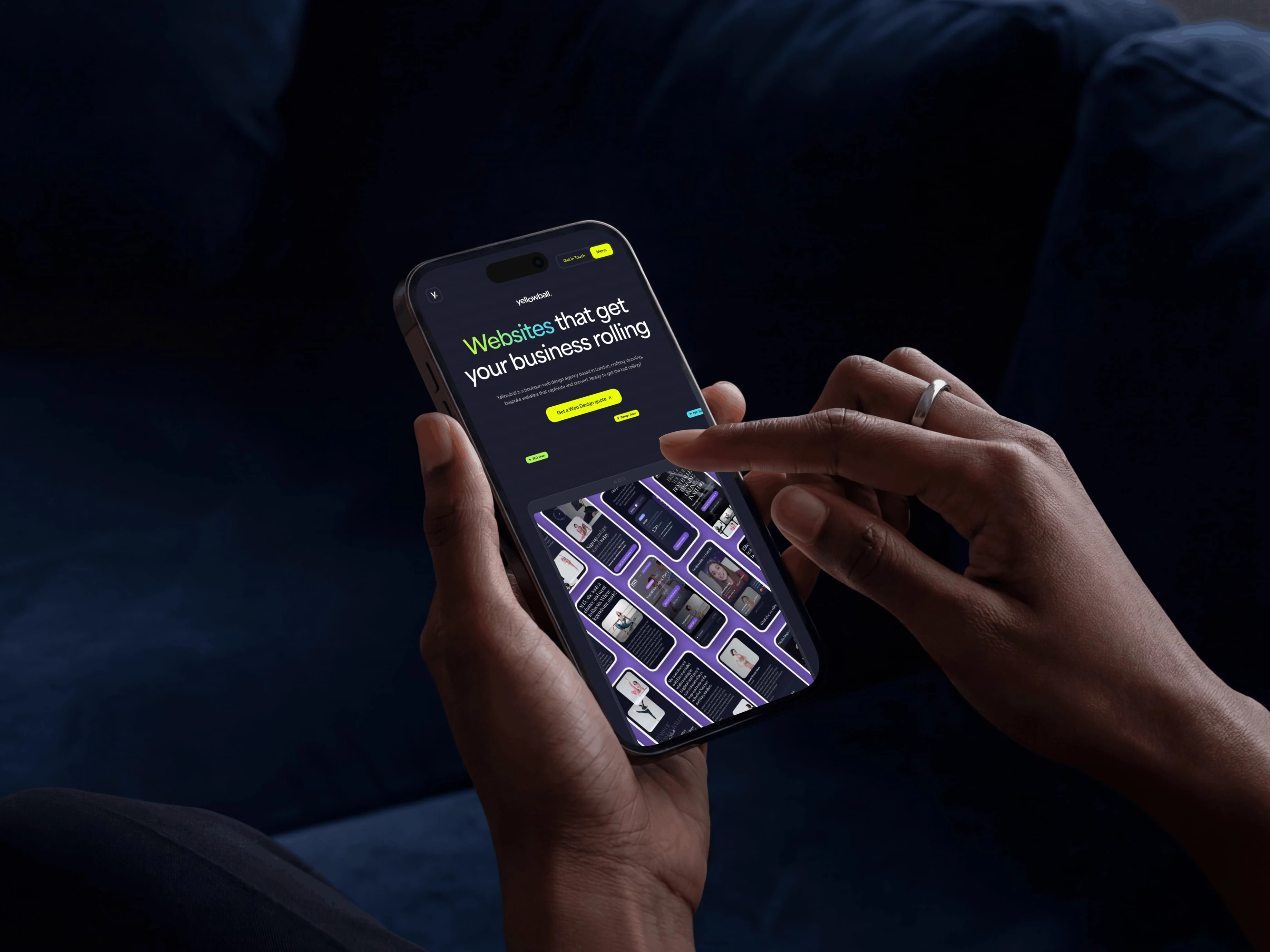 Person holding a smartphone displaying a web design app, with a finger pointing at the screen, against a dark background.
