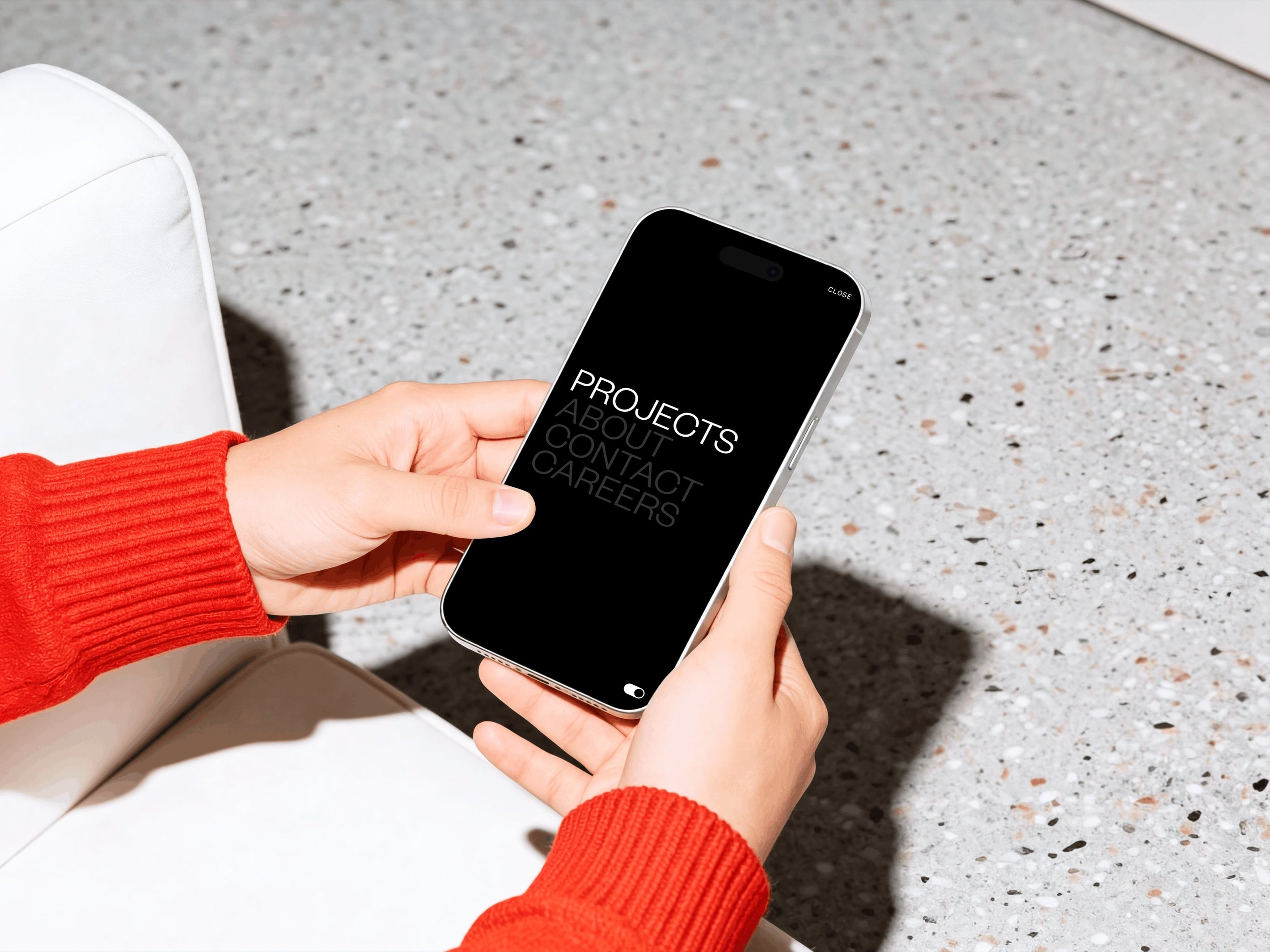 Person in a red sweater holding a smartphone displaying the words "PROJECTS ABOUT CONTACT CAREERS" on a black screen.