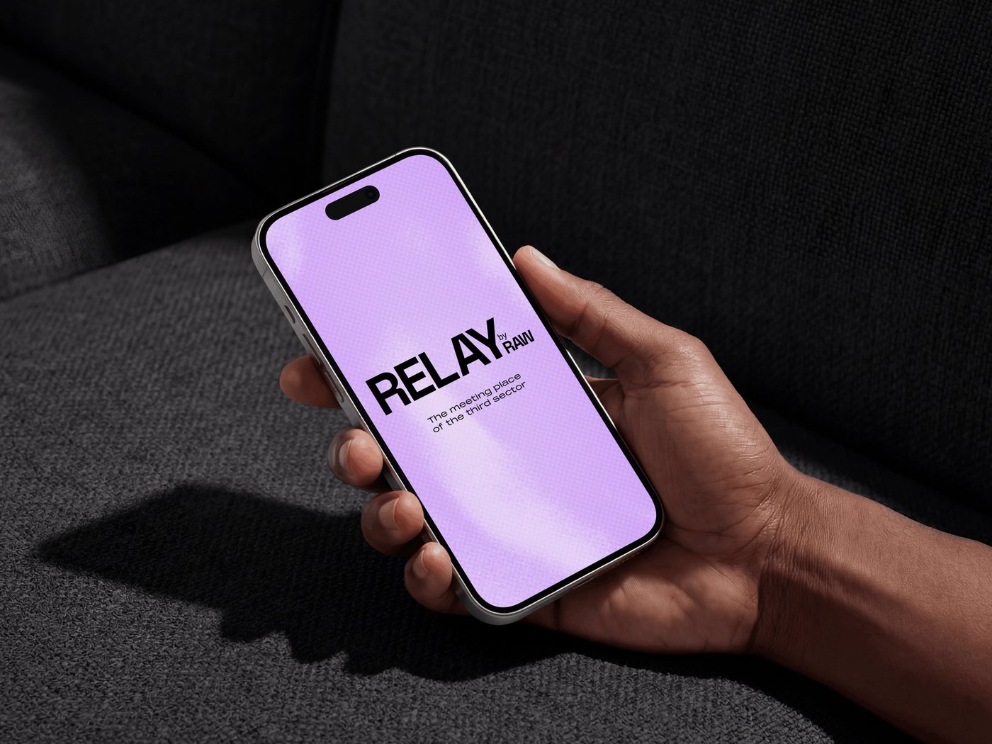 A hand holds a smartphone displaying a purple screen with the word "RELAYRAW" in bold black text, set against a dark background.