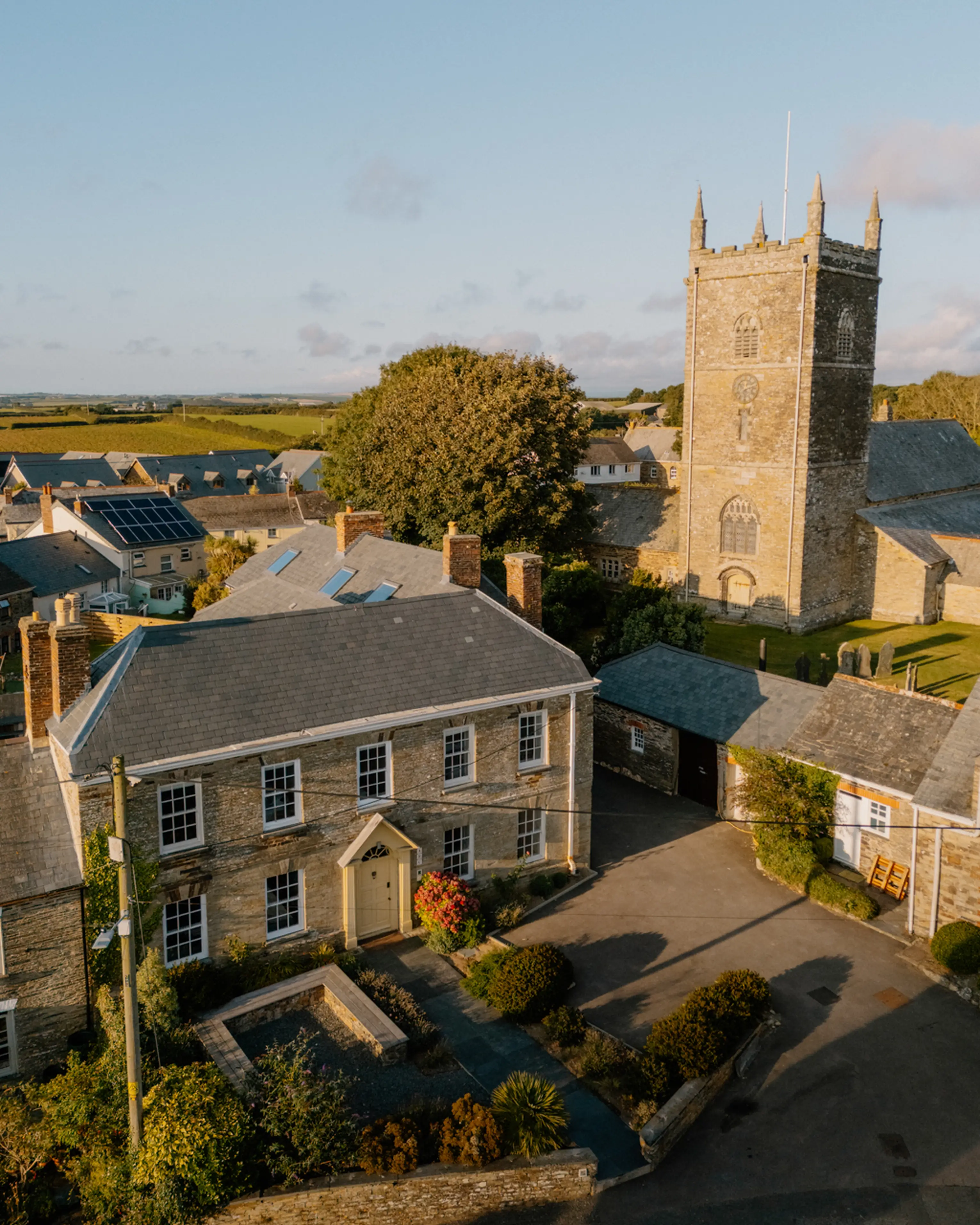 Aerial view of ARC Padstow among the rooftops of St Issey village with the church tower alongside