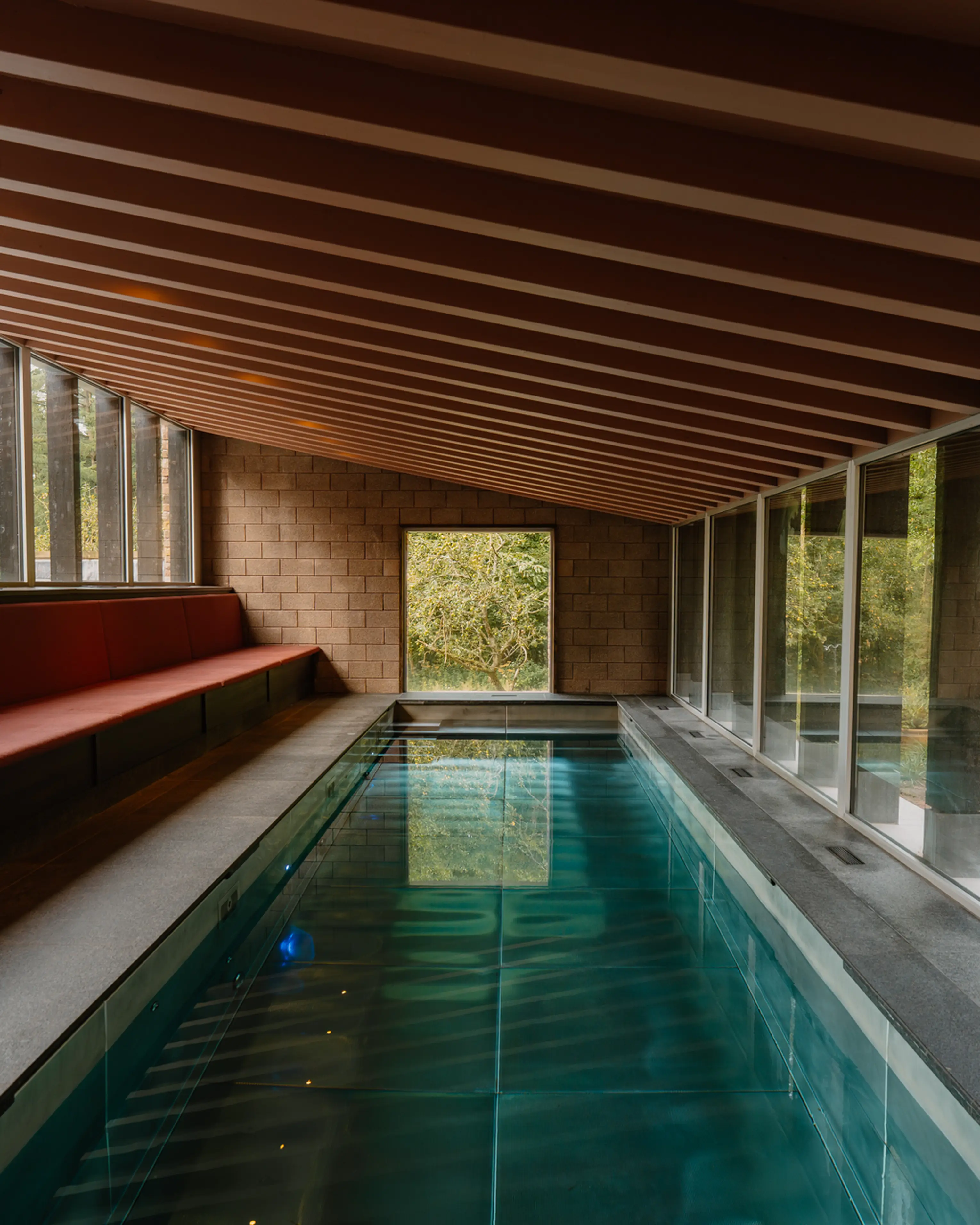 The indoor pool at ARC Peaks lit at dusk beneath a timber ceiling, with glass onto the garden