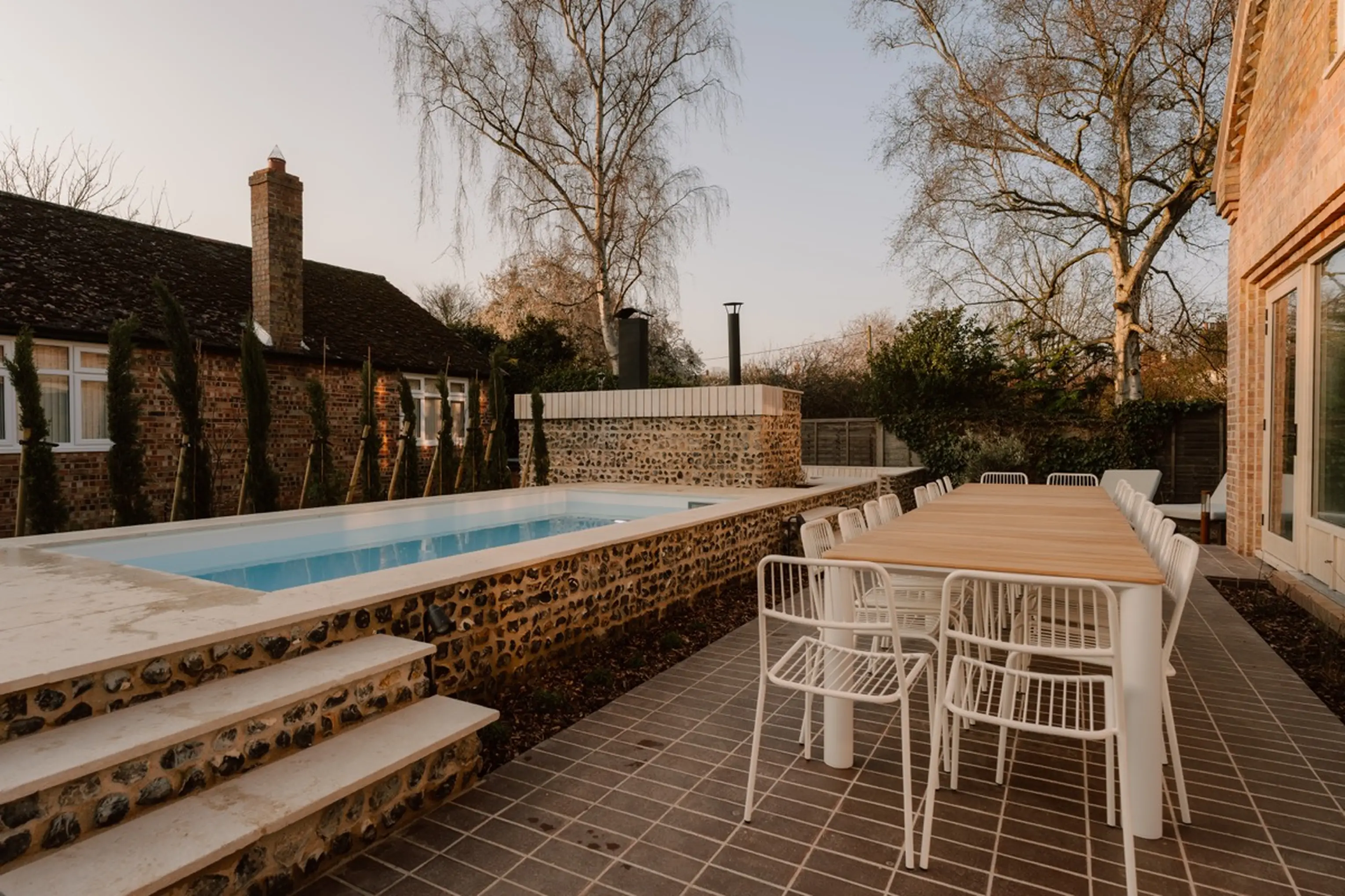 Pool terrace at ARC Next-the-Sea with an outdoor dining table beside a brick wall