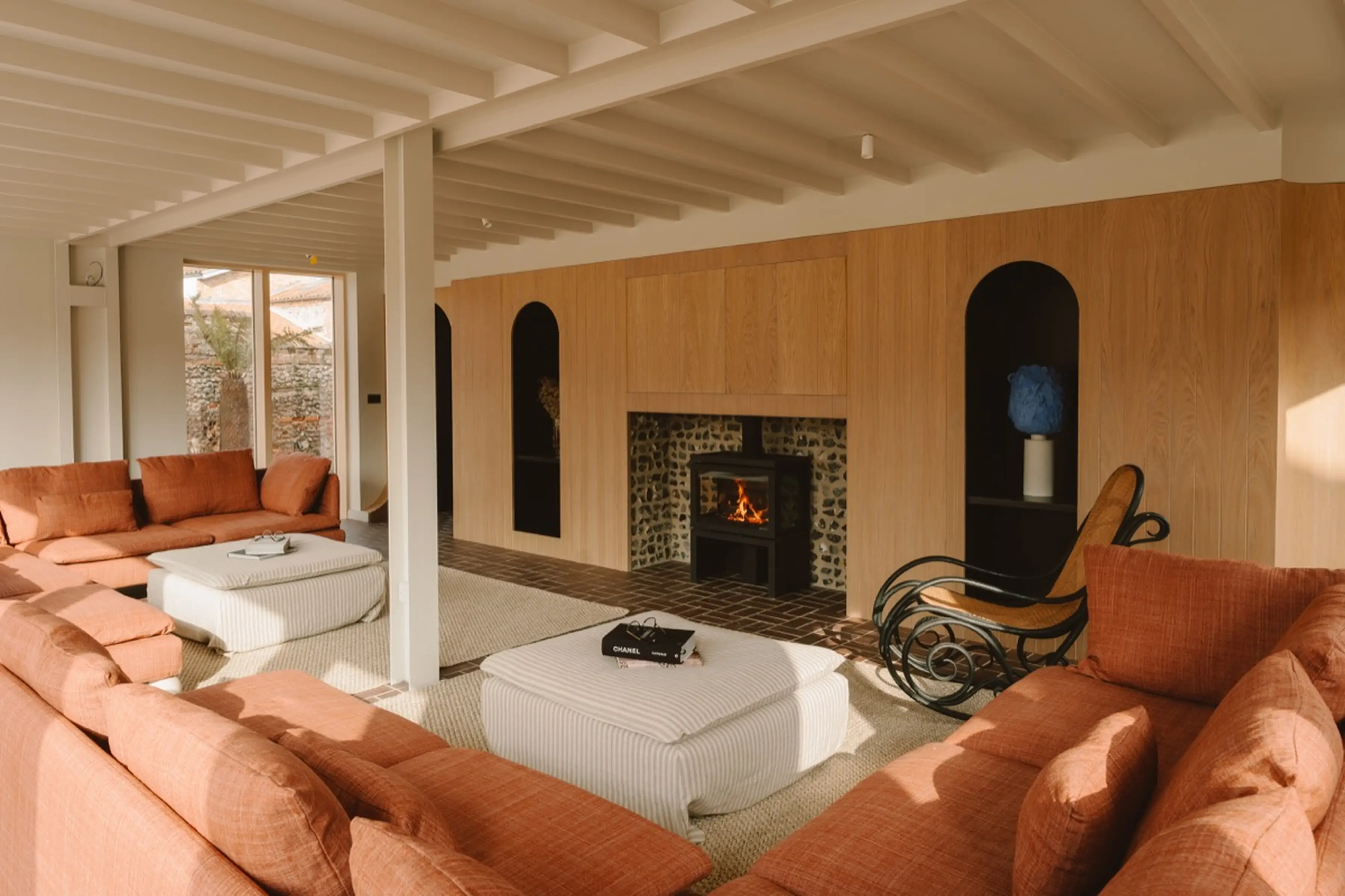 Open-plan living room at ARC Next-the-Sea with terracotta sectional sofas, a fireplace and a beamed white ceiling