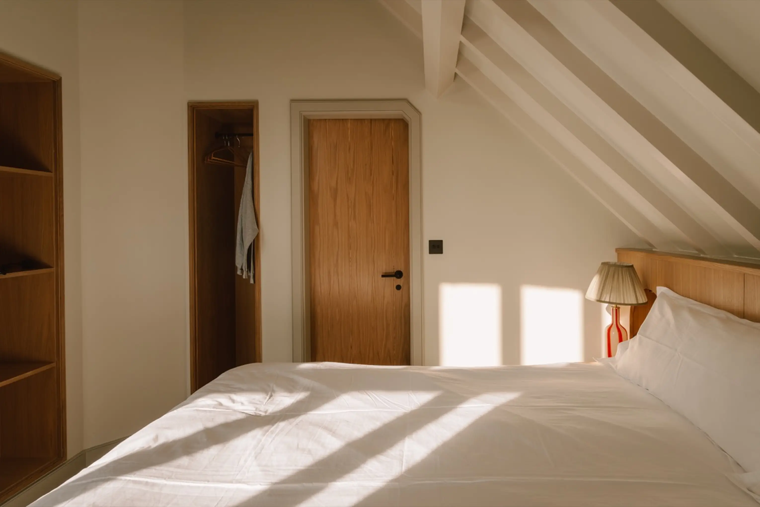 Bright eaves bedroom at ARC Next-the-Sea with a timber door and white bed