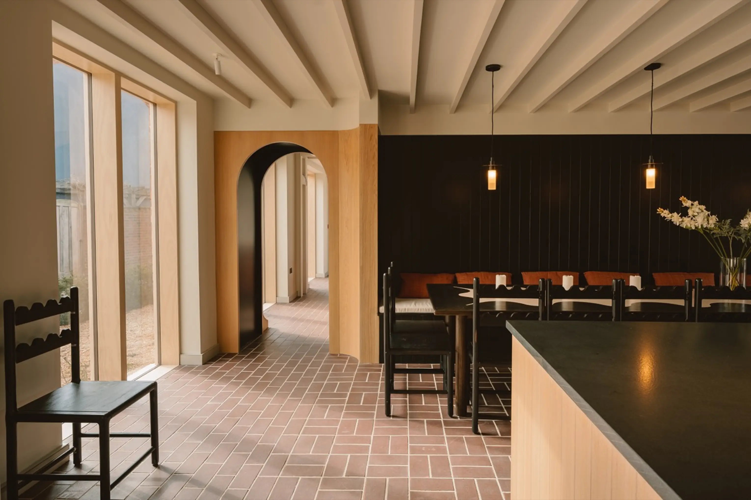 Dining area at ARC Next-the-Sea with a long table, an arched doorway and a dark panelled wall