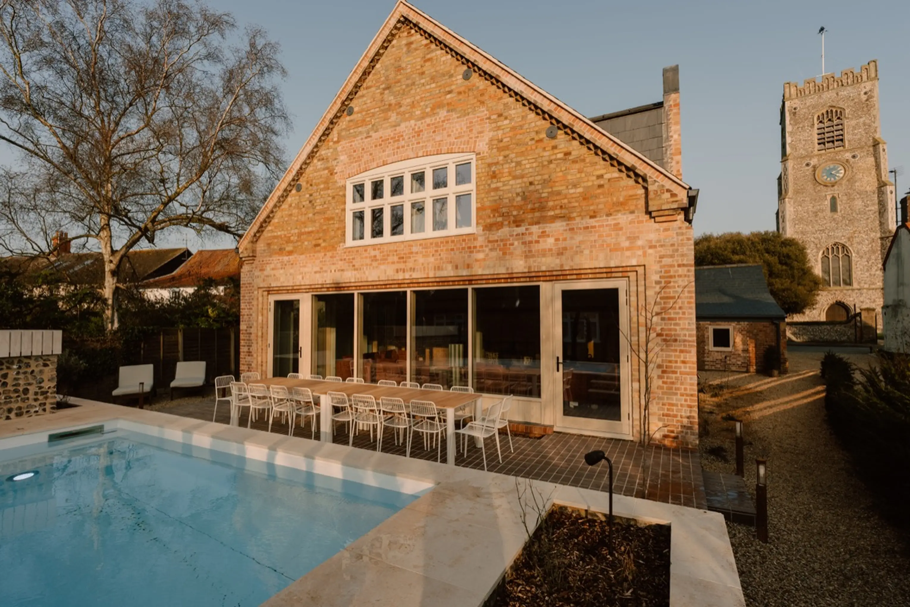 Outdoor pool and sun deck at ARC Next-the-Sea with the brick house and church tower behind