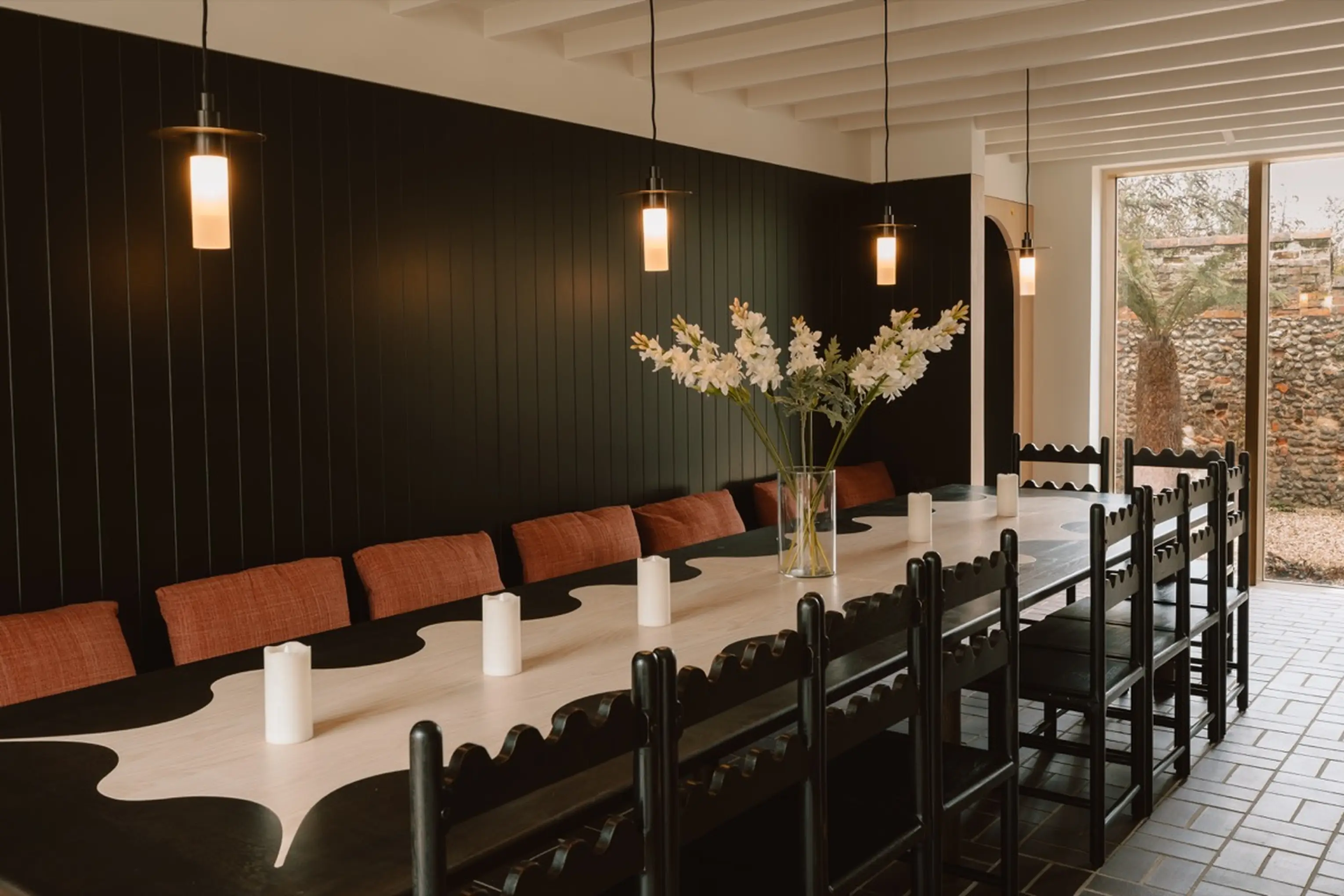 Long dining table laid for a group at ARC Next-the-Sea against a dark panelled wall