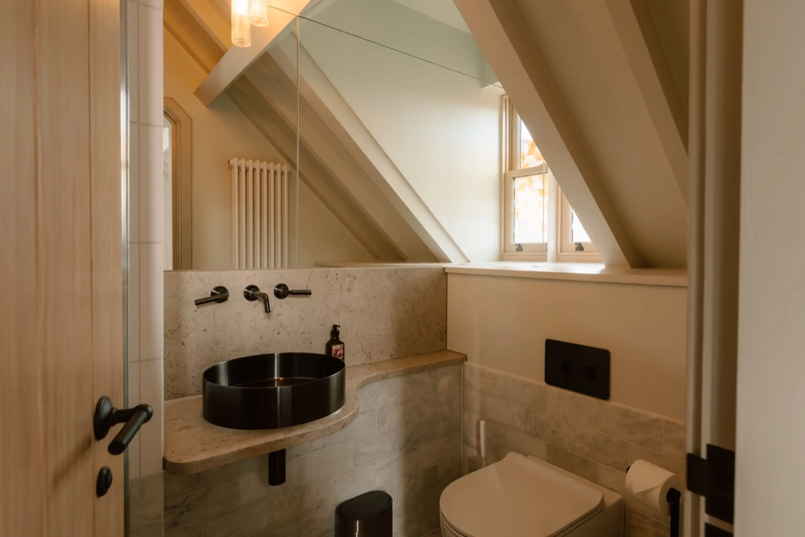 Ensuite under the eaves at ARC Next-the-Sea with twin black basins and exposed beams
