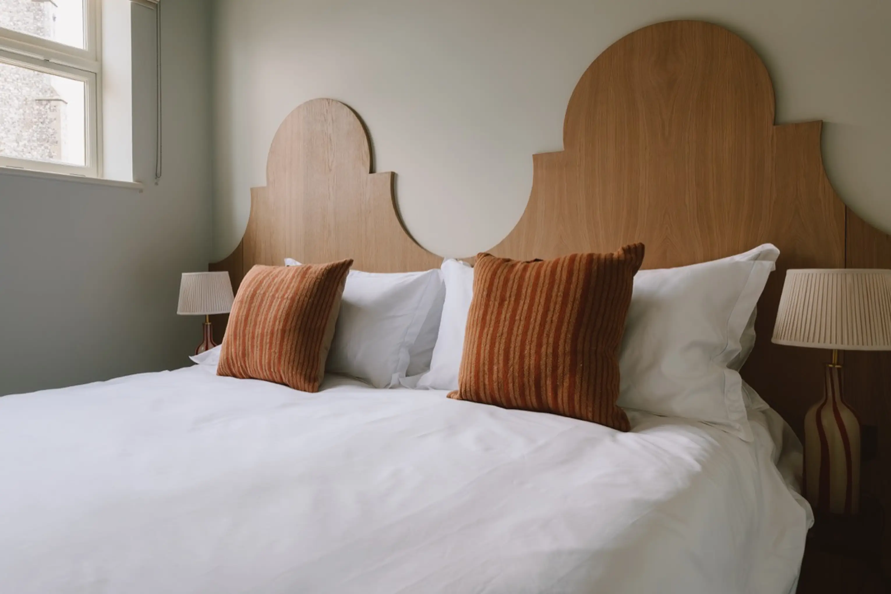 Bedroom at ARC Next-the-Sea with a curved timber headboard and terracotta cushions