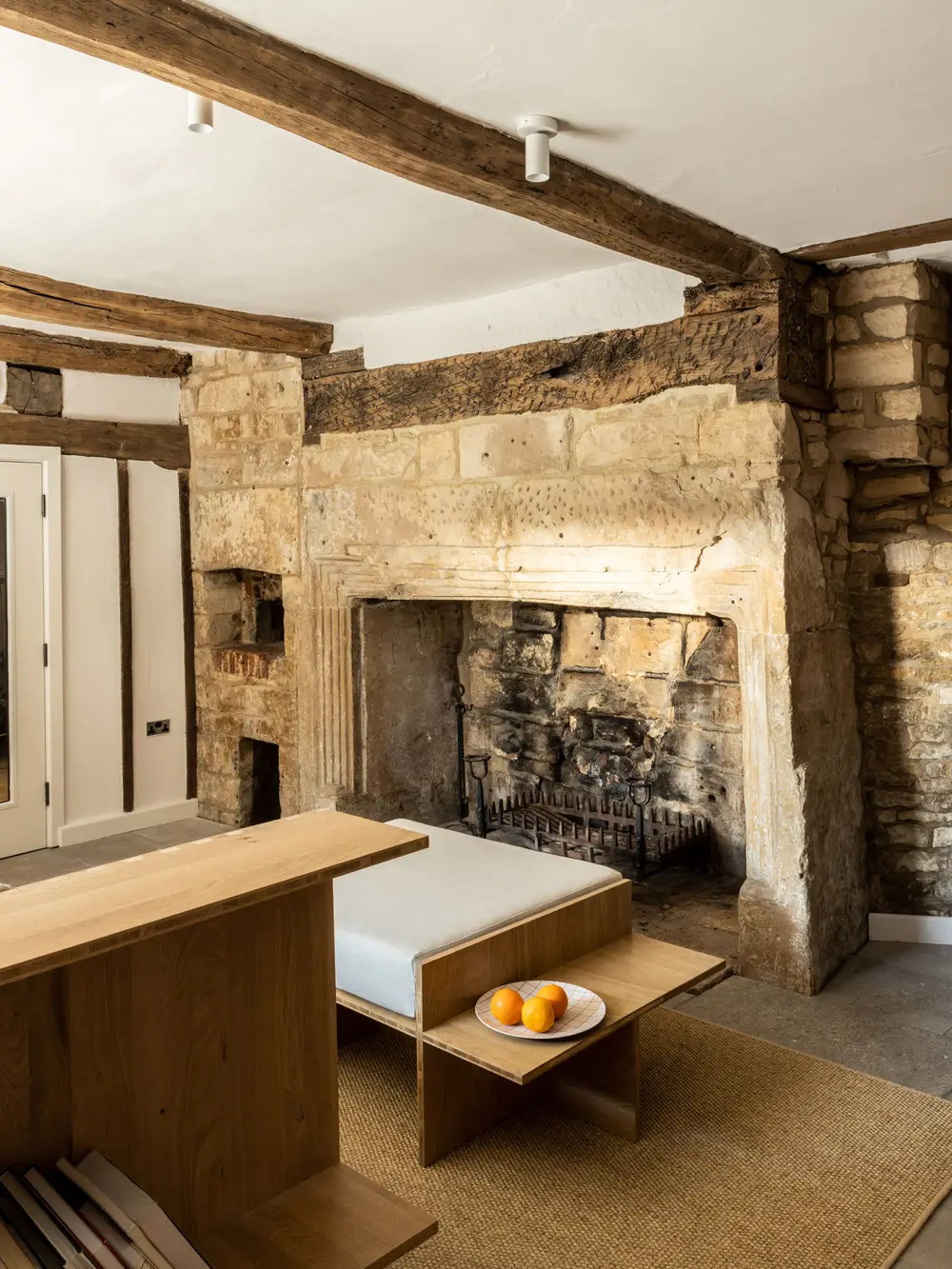 A rustic room with a large stone fireplace, wooden beams, and a minimalist wooden bench available for large groups staying at ARC Painswick.